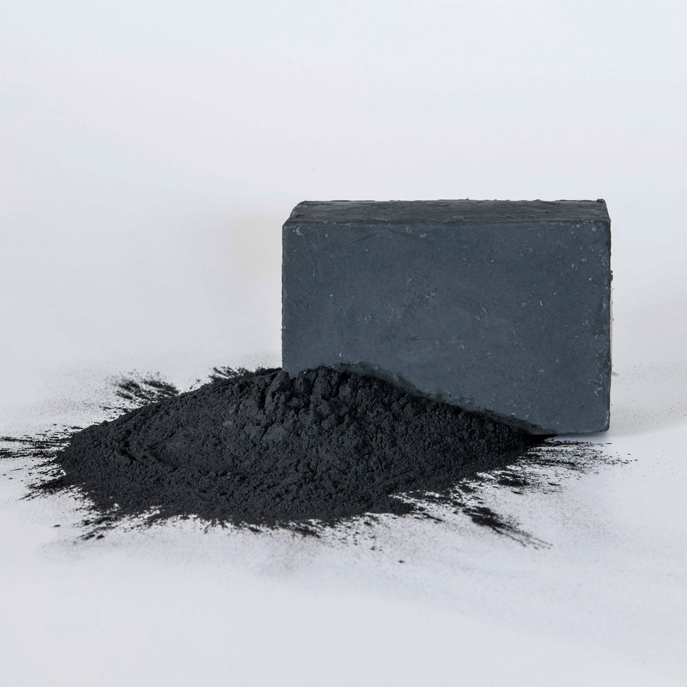 Bar of charcoal soap on a textured surface with a purple background