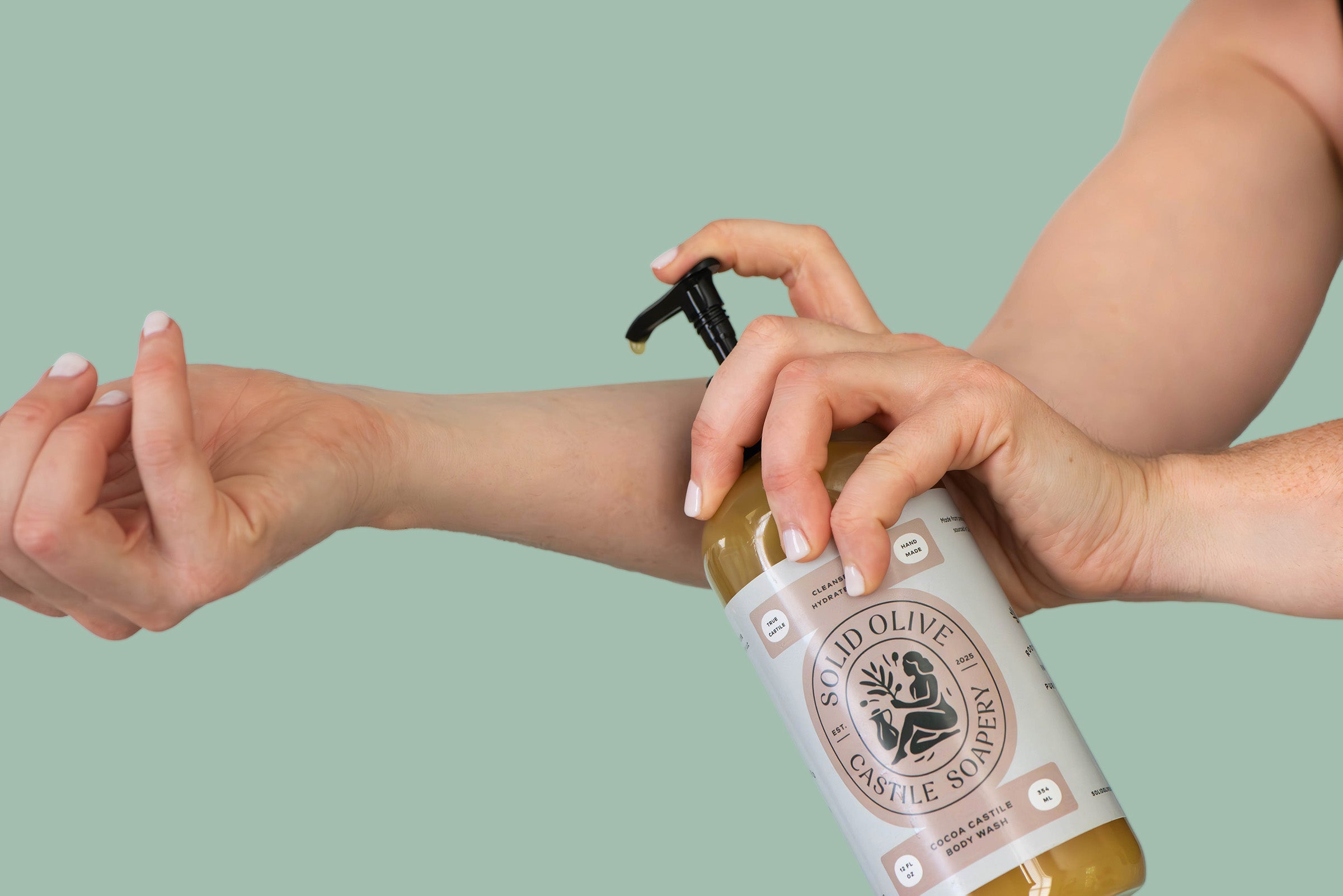 Person applying olive oil from a bottle labeled 'Real Olive Oil' on their arm against a green background