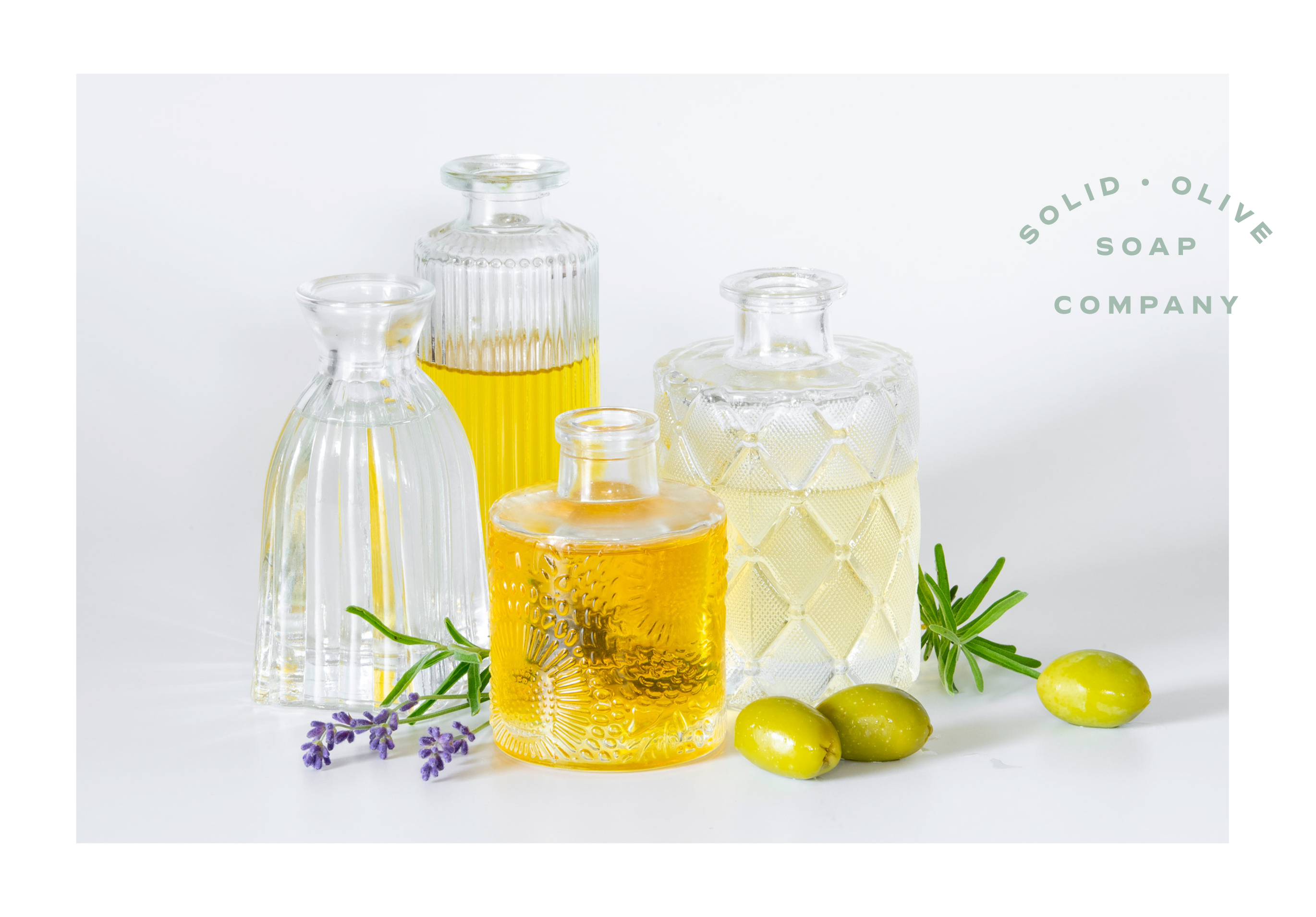 Four small bottles of essential oil surrounded by lavender and olives.