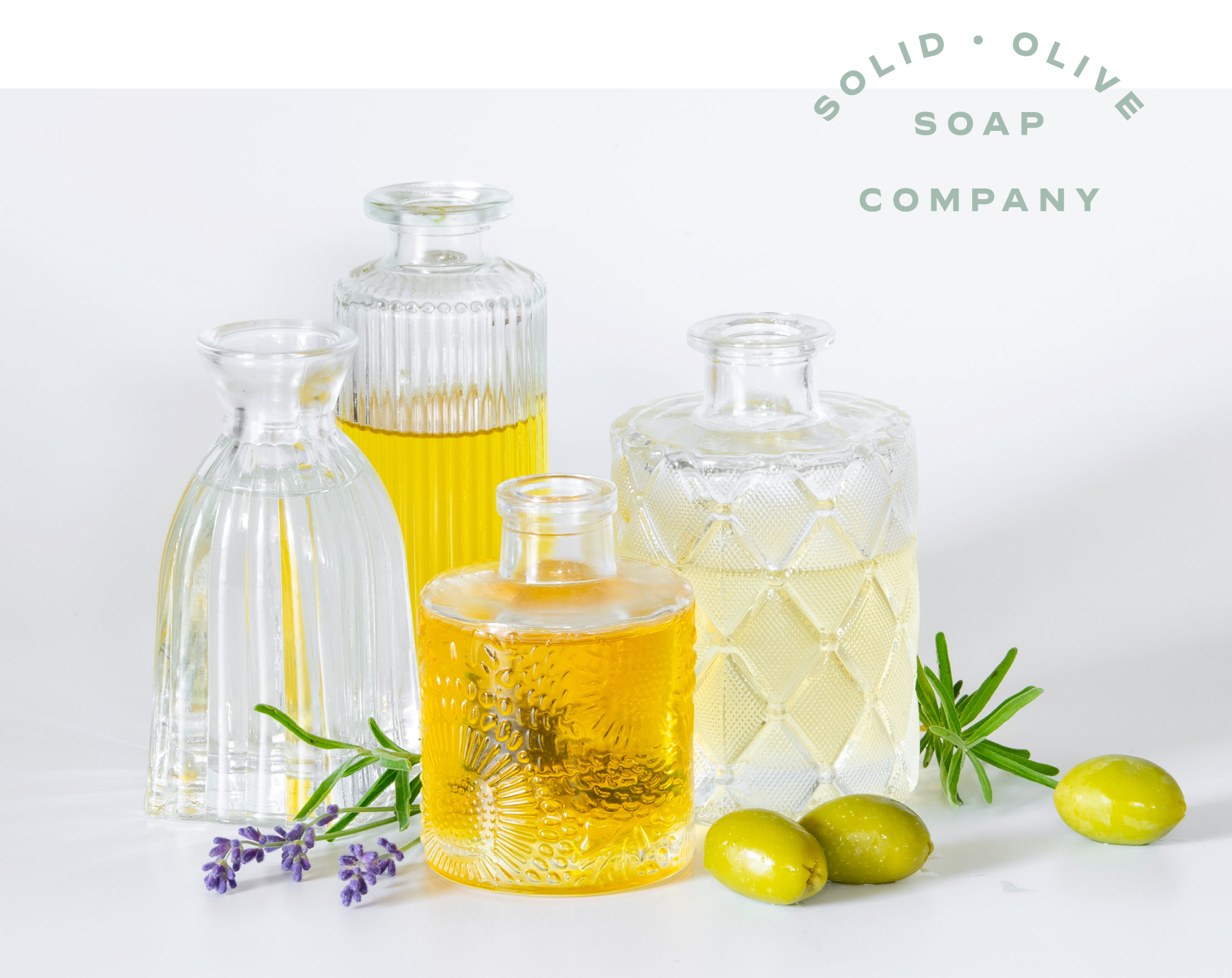 Four small bottles of essential oil surrounded by lavender and olives.