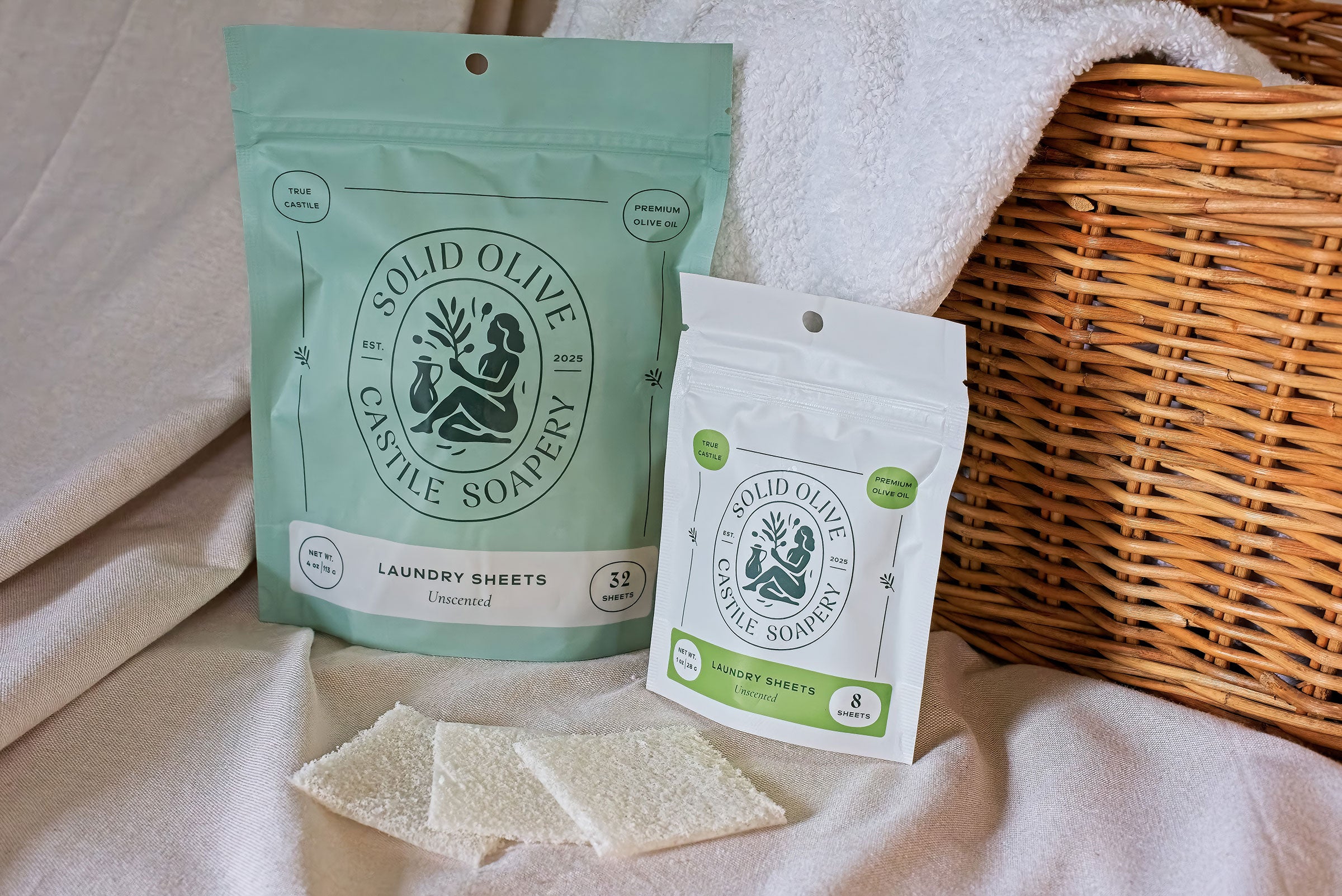 Two bags of laundry sheets sit on a linen cloth against a wicker basket. A towel peaks over the basket, and three laundry sheets sit in front of it.