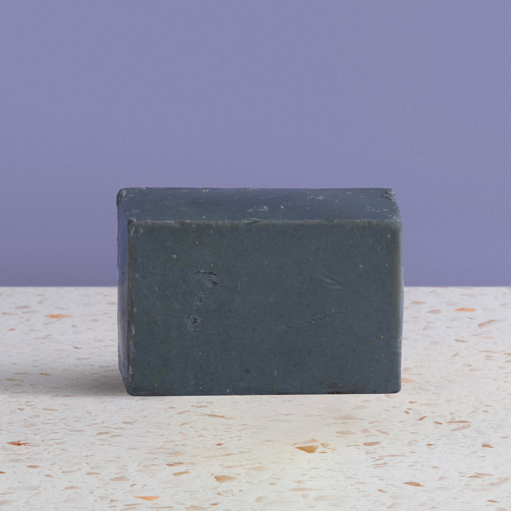 Bar of charcoal soap on a textured surface with a purple background