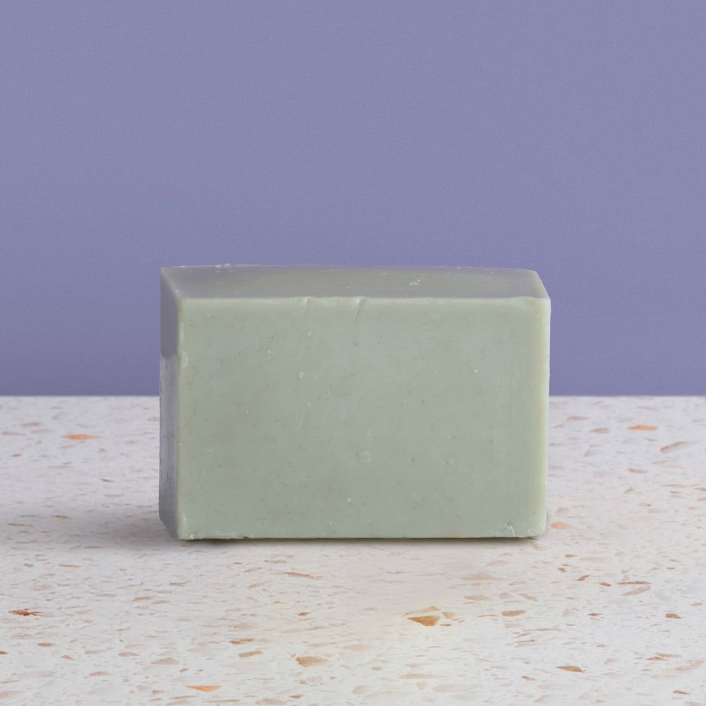 bar of french green soap on a speckled surface with a purple background