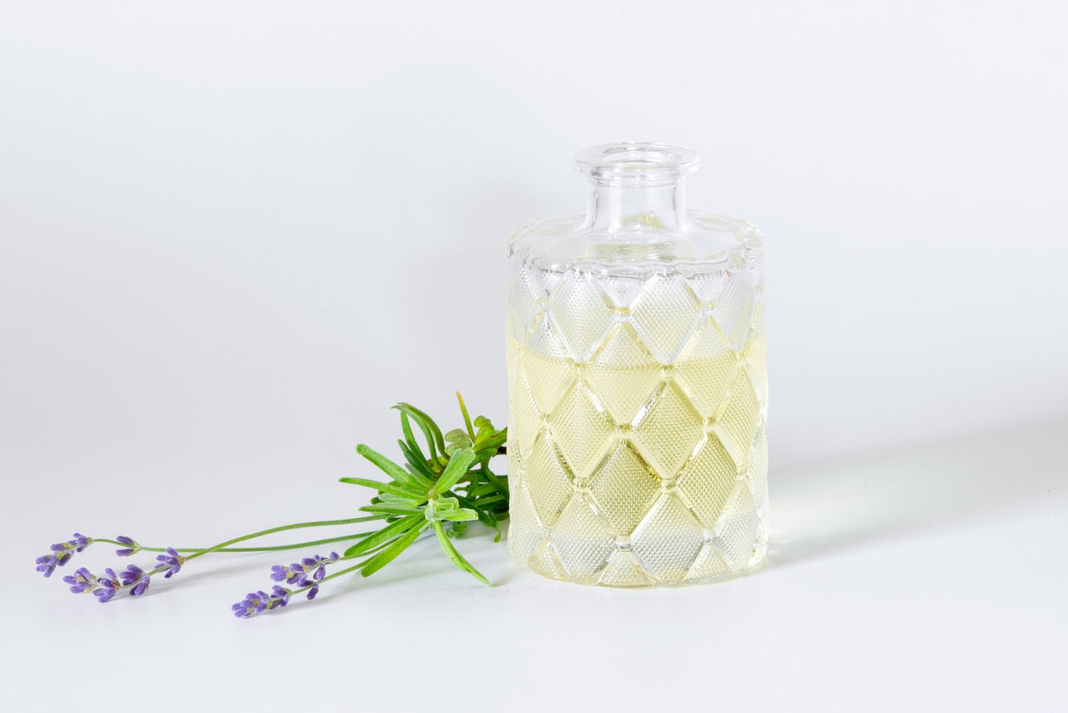 Lavender sprigs beside a textured glass bottle of pale golden oil