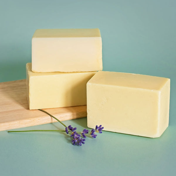 Three bars of lavender scented baby soap sit on a green background. Lavender flowers lay in front of them.