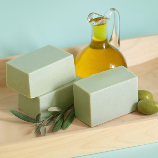 Three bars of green soap with a glass container of olive oil on a wooden surface.