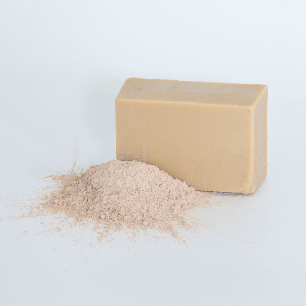 Bar of rhassoul soap on a textured surface with a purple background