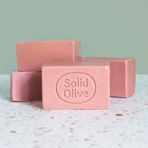 Four bars of rose pink Castile soap on a terrazzo countertop. One has the Solid Olive logo on it.