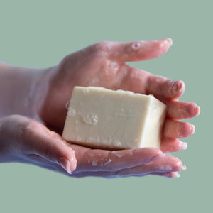 A woman's hands hold a bar of unscented castile soap. Both have soap suds on them.