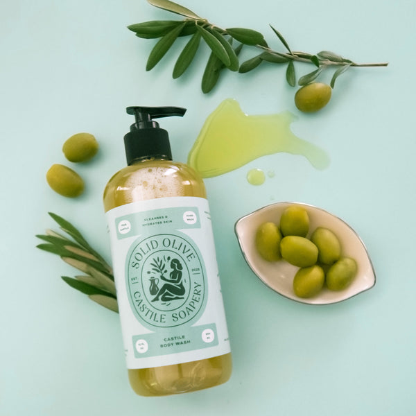 Bottle of Solid Olive & Castile Soapery product with olives and olive branch on a light blue background