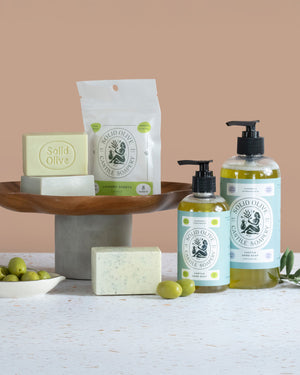 Solid Olive Castle Soaps products including soap bars, liquid soap, and a bar of soap on a wooden stand with a beige background.