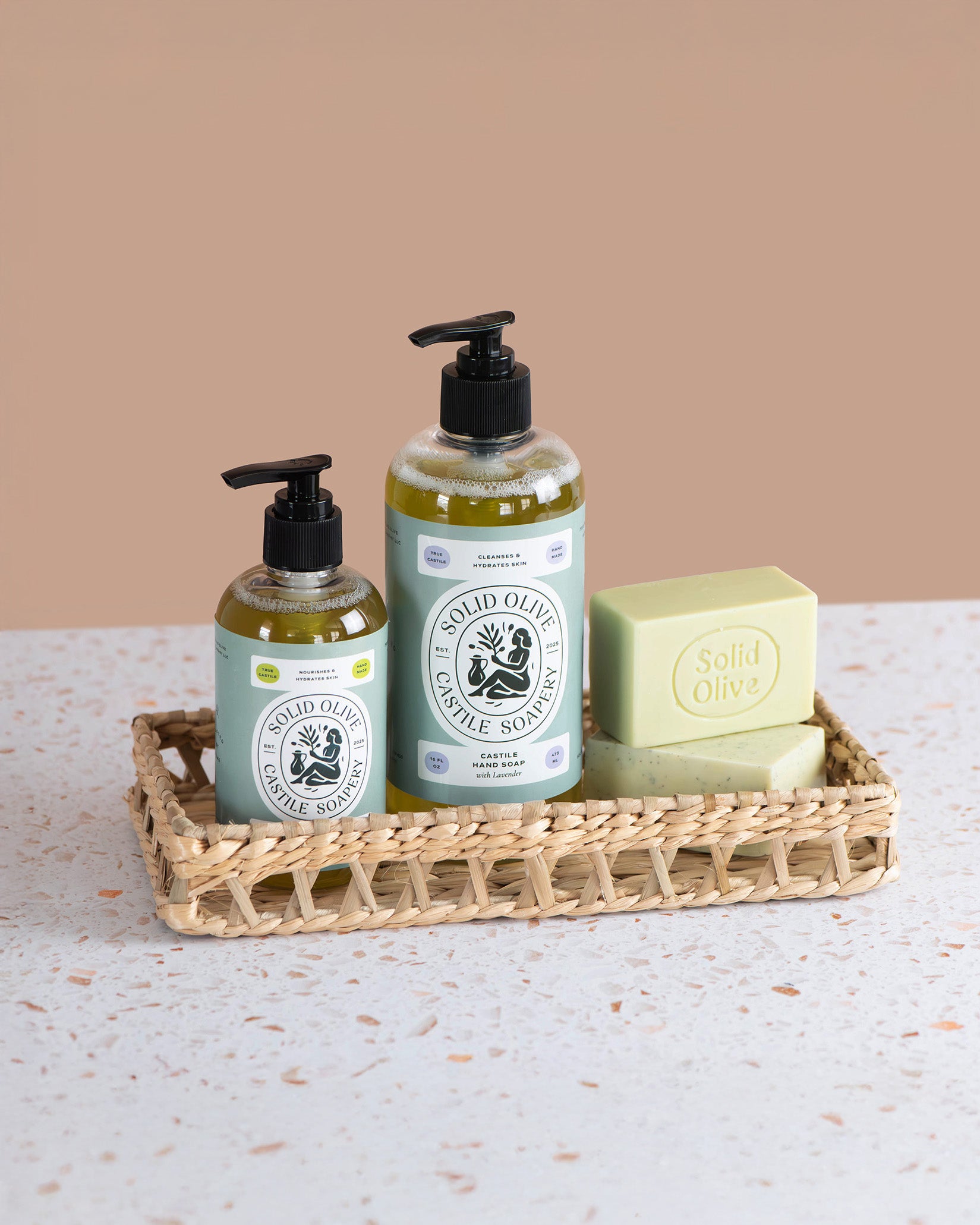 Two bottles of Solid Olive soap and a bar of soap on a woven tray with a beige background.