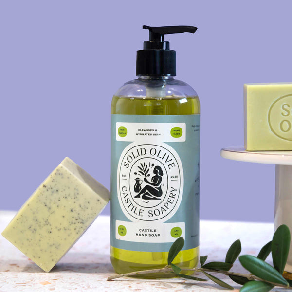 Bottle of Solid Olive Castile Soap with two bars of soap and olive leaves on a light purple background