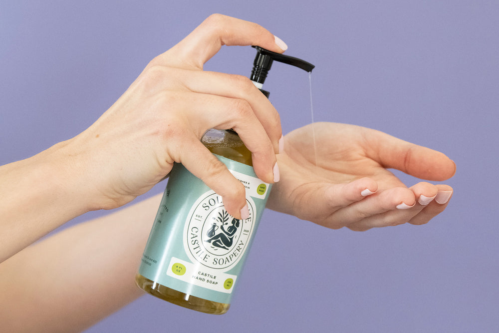 Person using a bottle of olive oil soap with a pump on a purple background