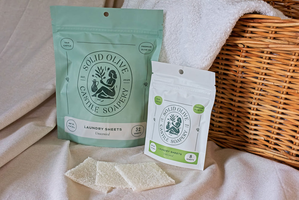 Two bags of laundry sheets sit on a linen cloth against a wicker basket. A towel peaks over the basket, and three laundry sheets sit in front of it.