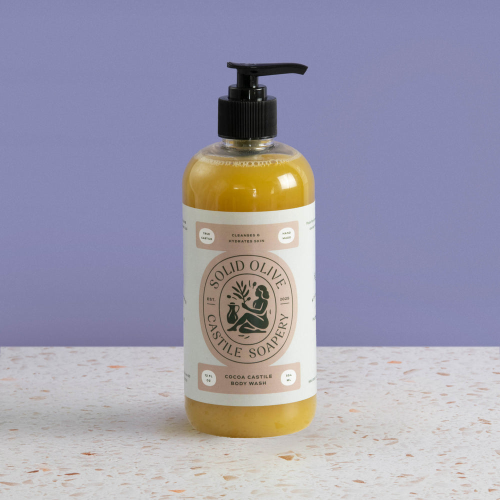 Solid Olive & Castle Soapery body wash bottle on a textured surface with a purple background