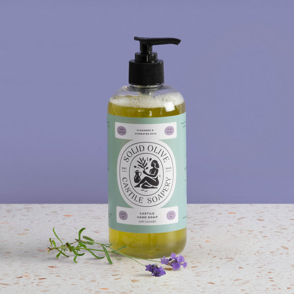 Bottle of Solid Olive & Castile Soapery hand soap with a pump on a textured surface and purple background