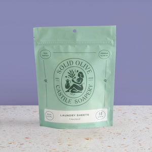 Green package of Solid Olive Castile Soapery laundry sheets on a light surface with a purple background