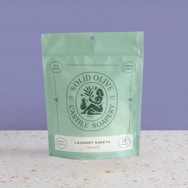 Green package of Solid Olive Castile Soapery laundry sheets on a light surface with a purple background