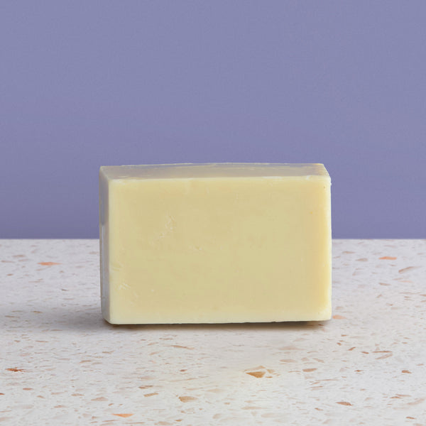 Bar of baby soap on a textured surface with a purple background