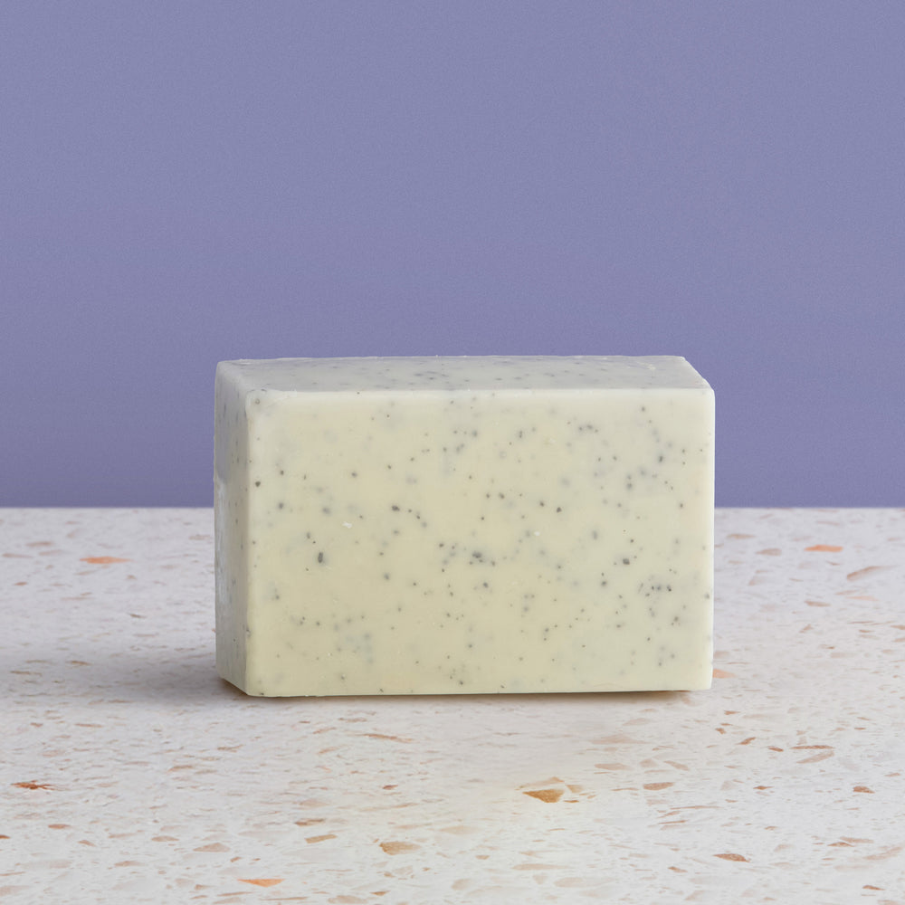 Bar of black sea salt soap on a textured surface with a purple background