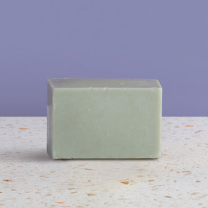 bar of french green soap on a speckled surface with a purple background