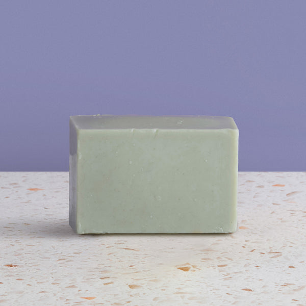 bar of french green soap on a speckled surface with a purple background