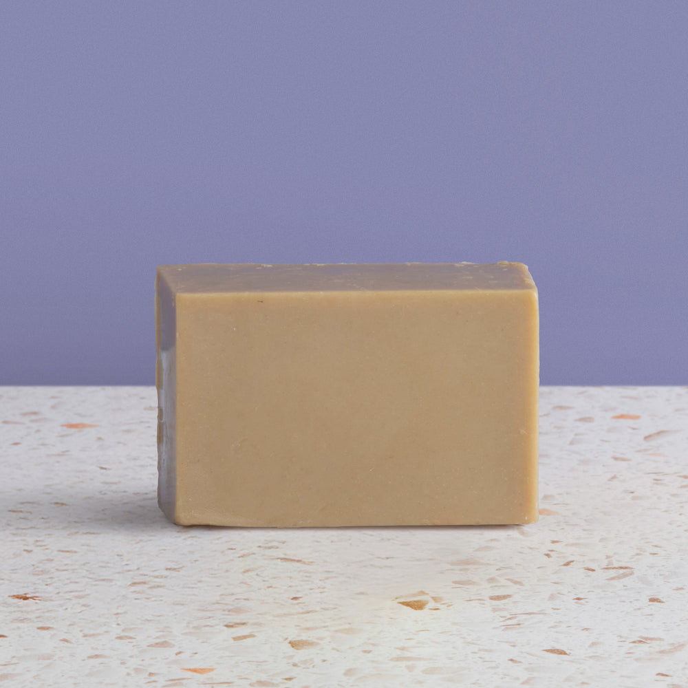 Bar of rhassoul soap on a textured surface with a purple background