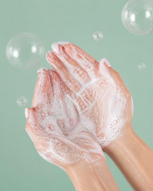 Hands with creamy lather against a sage green background