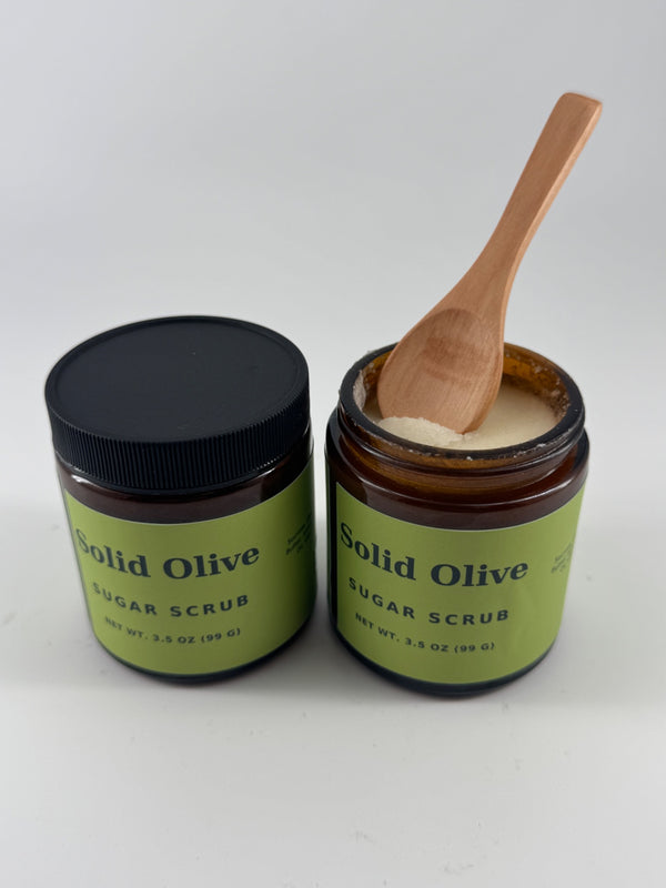 Solid Olive 3.5 oz sugar scrub in amber glass jars, with an open jar showing the scrub texture